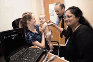 Study volunteer Catherine Miele holds her son Robert as K. Vadivu, MD (right), a visiting obstetrician/gynecologist from India, practices scanning techniques.